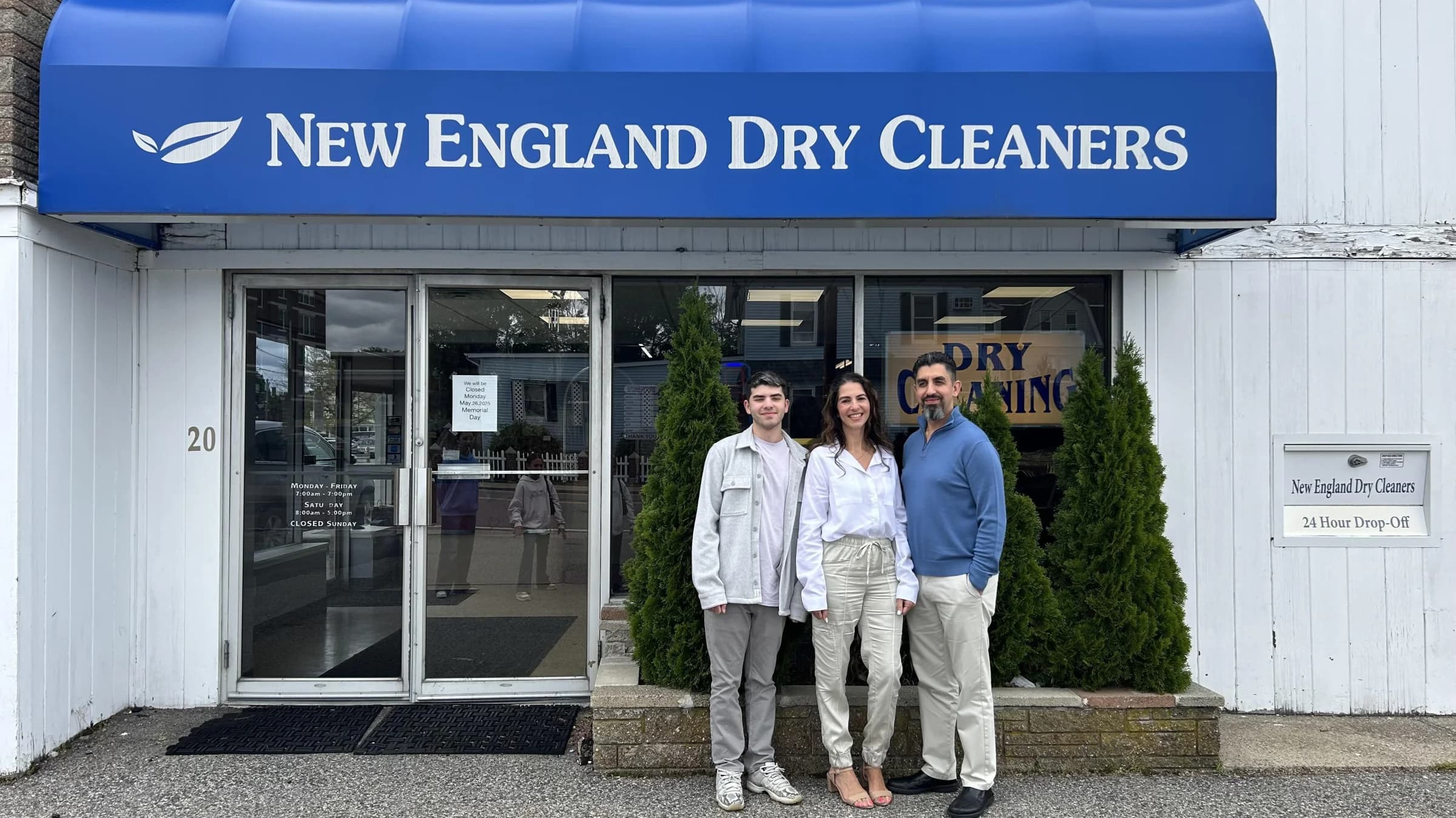 The New England Dry Cleaners storefront at 20 Elm Street, the navy awning, glass door, and the family in front